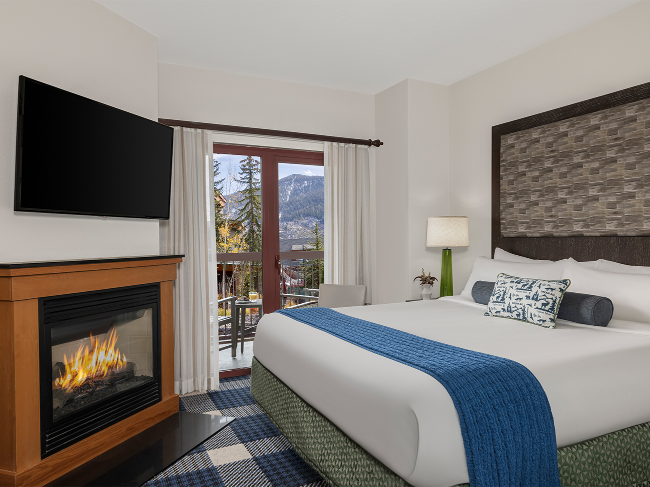 A cozy and inviting bedroom at the Marriott Grand Residence Club, Lake Tahoe, featuring a warm fireplace and a stunning view of the majestic mountains in the background.
