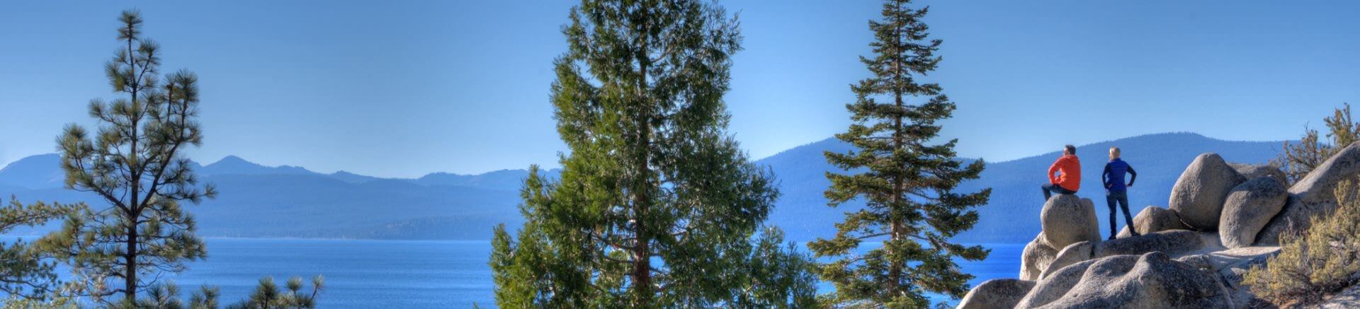 Two hikers enjoying the scenic view of Lake Tahoe with trees and mountains in the background